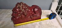 Left side of red and gold ceramic lion next to measuring tape