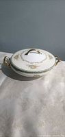 Covered porcelain serving bowl with lid in profile showing floral band and gilt handles