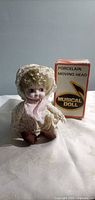 Front view of porcelain musical doll beside original box