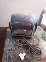 Front view of chrome roll-top toaster with cord