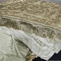 stack of metallic damask tablecloth atop pile of ivory linens