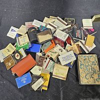 Pile of assorted vintage matchbooks and two holders on black surface