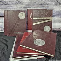 Group of six+ maroon hardcover yearbooks standing and lying flat