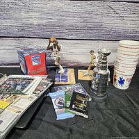 Overview of lot showing trading cards, sealed packs, NBA figurines, Stanley Cup replica and cups