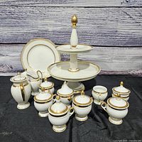 Group shot of all porcelain pieces including stand, plates, covered cups, creamer and sugar