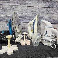 Two steam irons, handheld steamer, measuring cup, plastic stands