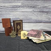 Group shot of all items: wood bookends, hardbound book, metal ship, relief bookend, stack of pamphlets