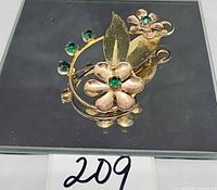 Front view of brooch showing floral design, mixed metal tones and green stones