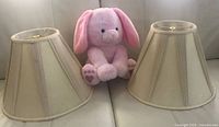 Two beige fabric lamp shades and one pink plush rabbit toy on sofa