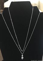 Two sterling silver pendant necklaces displayed on black bust