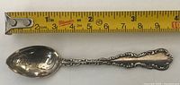 Full view of sterling silver souvenir spoon beside tape measure, showing length