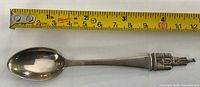 Full view of sterling silver souvenir spoon beside tape measure showing length
