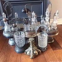 Overall view showing three silver-plated castor stands, glass bottles, pressed-glass jars and detached base