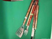 Group shot of all four wood-handled BBQ utensils on green background