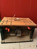 Front view showing Workmate ShopBox branding, wood top, red clamp pegs