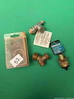 All four plumbing items laid out including blister pack, Y-splitter, Gilmour connector, metal T valve