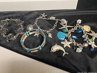 All four bracelets and loose dolphin charm laid out on black fabric