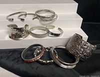 Full group of silver-tone cuffs and bangles displayed on steps
