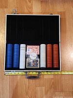 Open aluminum case showing chips, cards, dealer button and dice with tape measure for scale
