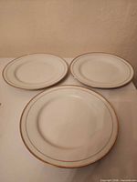 Three white porcelain plates with gold rims laid out