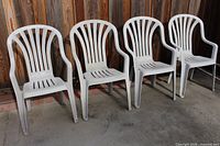 All four white plastic chairs lined in a row against wooden fence