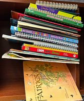 Stack of spiral-bound and softcover children’s books in shelf showing multiple titles
