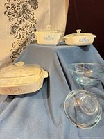 Group shot showing all three CorningWare casseroles with lids, two Pyrex bowls, and lids