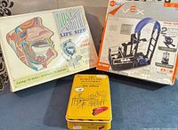 Group shot of all three boxed items: anatomy kit, VEX kit, card game tin