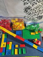 Assorted Duplo bricks in bags, slide tracks, baseplate and car chassis with figure displayed