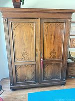 Front view of antique solid wood armoire showing double carved doors and overall design