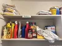 Shelf with assorted trigger-spray cleaners, pour bottles, paint can, rags