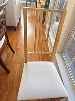 Front view of light wood chair showing slatted back and white seat