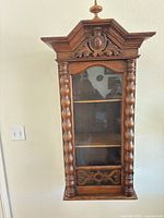 Front view showing carved crest, glass door, shelves