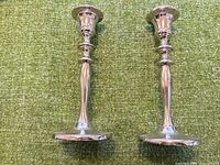 Two polished silver metal candlestick holders standing upright on green fabric