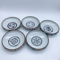 Group shot of five Arita Imari shallow bowls showing varied central motifs and gilt-rimmed edges