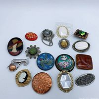 Group shot of all sixteen brooches showing variety of shapes, sizes and finishes