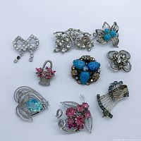 Front view of nine assorted silver-tone brooches showing stone colors and designs