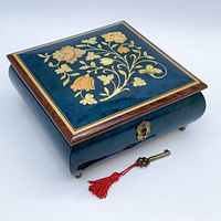 Closed box angled view showing floral inlay, blue-green lacquer, brass key and tassel