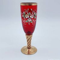 Full view of ruby red champagne flute with floral enamel and gold stem