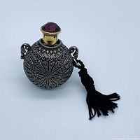 Full view of ornate spherical perfume vial pendant with red gem cap and tassel