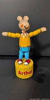 Front view of wooden Arthur push puppet on yellow base