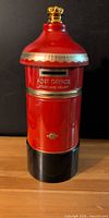 Front view of red pillar box coin bank showing text and coin slot