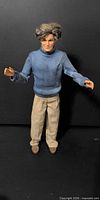 Front view of Ken doll standing in blue sweater and beige pants