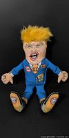 Front view of Donald Trump plush dog toy in blue suit with yellow hair