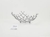 Oblique view of chrome wire basket showing overall shape and three ball feet