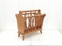 Angled front view of wooden magazine rack showing spindle dividers, legs and finish