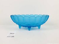 Full side view of blue satin oval footed bowl showing scalloped rim and four feet