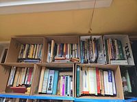 Six cardboard boxes filled with assorted hardcover and paperback books across multiple genres.