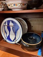 Shelf showing blue wave plates in stand, pottery bowl, floral tureen with cup and saucer above