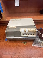 Front view of Wollensak 1500 tape recorder with lid on and accessories beside